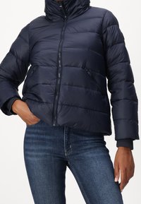 Giubbotto imbottito blu navy con colletto alto, chiusura a zip e polsini elasticizzati. Presenta cuciture orizzontali e tasche laterali.