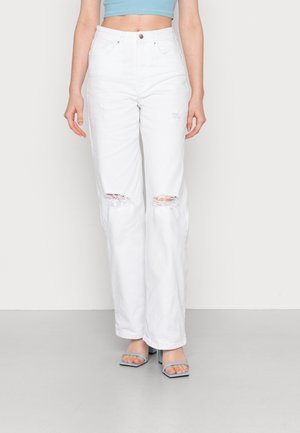 Jeans de mezclilla blancos desgastados con rodilleras rasgadas, cintura alta y un ajuste holgado, combinados con tacones destalonados azules y un top corto a juego.