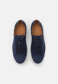 Marinblå sneakers med en texturerad ovandel, med bruna accenter på det inre foderet och vita gummisålar. Snörning med sex öglor.