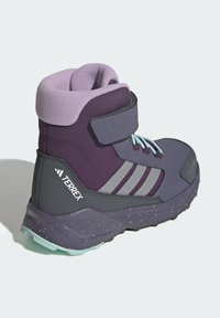 Purple hiking boot with a textured upper, velcro strap, and grey accents. It has a speckled sole and light blue laces for contrast.