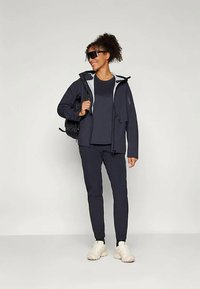 Námornícká venkovní bunda se světlým šedým interiérem, doplněná odpovídajícím tričkem a kalhotami. Bílá sportovní obuv dotváří celkový vzhled.