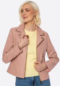 Giacca in pelle rosa chiaro con chiusura a zip, colletto a scatto e dettaglio trapuntato sul lato, indossata sopra una maglietta gialla e abbinata a jeans blu.