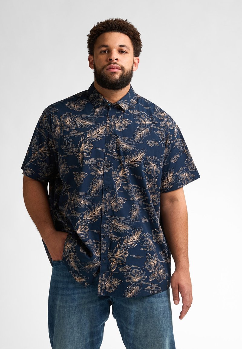 Marineblauwe overhemshire met een tropisch bloemenpatroon in gouden tinten, korte mouwen en een relaxed fit, gecombineerd met blauwe jeans.