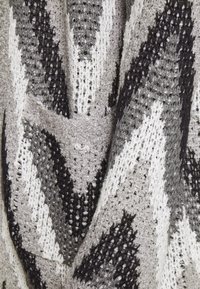 Tissu tricoté gris et noir avec motif en zigzag, comprenant des sections à tissage fermé et ouvert, créant une texture variée et un intérêt visuel.