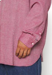Gestreiftes Langarmshirt in Rot und Weiß mit Knopfmanschetten, aus strukturiertem Stoff und mit seitlichen Schlitzen, kombiniert mit blauer Denim.