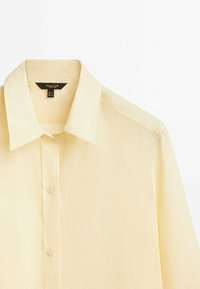 Chemise jaune boutonnée en tissu léger, avec un col classique, une rangée unique de boutons, et des manches droites et épurées.