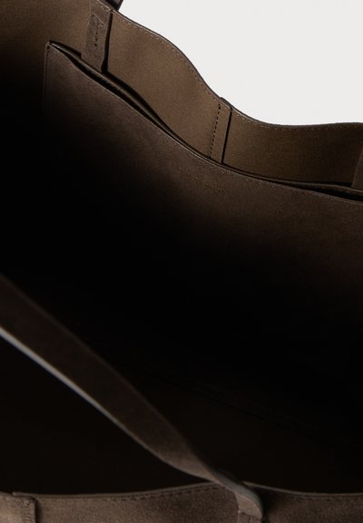 Καφέ τσάντα ώμου από σουέντ με απαλό υλικό, διαθέτει ανοιχτό πάνω μέρος και δύο εσωτερικά διαμερίσματα για οργάνωση. Υπάρχει διακριτική λεπτομέρεια με το λογότυπο.