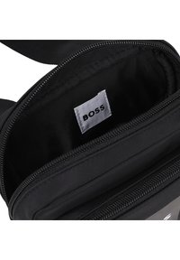 Μαύρο τσάντα χιαστί από ύφασμα με φερμουάρ, με εσωτερική λευκή ετικέτα «BOSS». Ομαλή υφή, ορθογώνιο σχήμα.