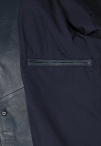 Marineblauwe jas met zacht leren en stoffen materiaal, met een ritszak en een gladde textuur aan de leren kant.