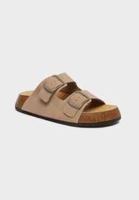 Sandalo slide in suede marrone con due fibbie regolabili, suola in sughero e suola in gomma testurizzata; design minimalista e stile aperto sul davanti.