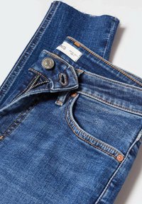 Blue denim jeans folded with partially unzipped zipper and visible metal button and front pocket stitching details.