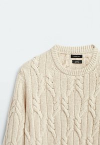 Sweterek w kolorze kremowym, dzianinowy, z okrągłym, prążkowanym dekoltem. Tekstura zawiera skręcone wzory i gładkie wykończenie. Metka widoczna na dekolcie.