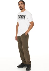 Witte katoenen t-shirt met een zwart "EXPLORE" grafisch ontwerp en tekst. Olijfgroene cargobroek met ritsen en zakken. Zwarte wandelschoenen.