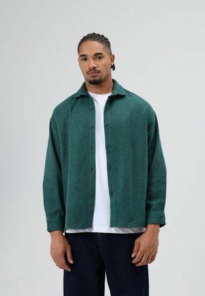 Groen overhemd met knopen, gemaakt van gestructureerde stof, met een kraag, lange mouwen en een losse pasvorm, gedragen over een wit t-shirt.