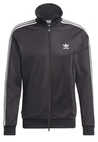 Svart zip-up jacka i slät tyg med vita tre-rands detaljer på ärmarna och en liten vit logotyp på bröstet.