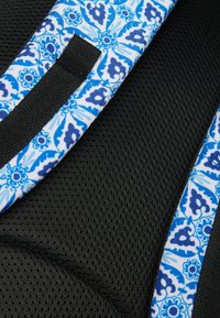Material de malla negra con acentos de tela azul y blanca estampada y correas negras. El diseño presenta un motivo floral con detalles intrincados.