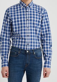 Camicia a quadri blu e bianchi con colletto, dotata di maniche lunghe. Abbinata a jeans in denim blu scuro.