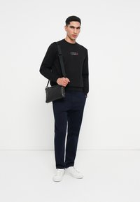 Μαύρο πουλόβερ με πολύχρωμο λογότυπο "Tommy Hilfiger", ναυτικές παντελόνες και μια μαύρη τσάντα messenger. Λευκά sneakers ολοκληρώνουν το σύνολο.