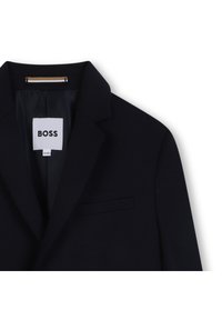 Marinblå blazer med slagkrage, enkel bröstficka och subtil textur. Har en BOSS-märkning i vitt och en gulddetalj vid halsen.