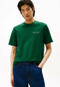 Grøn bomulds T-shirt med korte ærmer og rund hals, med et hvidt logo "TOMMY HILFIGER Etableret 1985" på brystet.