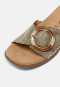 Sandale à bout ouvert avec semelle intérieure en daim beige et bride en daim vert olive clair avec une grande boucle ronde en écaille de tortue.