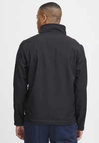 Zwarte softshell jack met hoge kraag en vlakke naden, met een gladde textuur en zonder zichtbare merknaam of zakken.