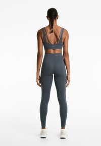 Sötétszürke sportmelltartó, hátrafelé keresztbe tett pántokkal, magas derekú sötétszürke leggings-szel párosítva. Mindkettő sima textúrájú.