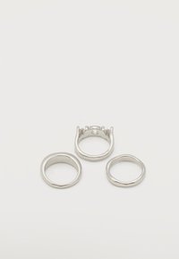 Τρία ασημένια δαχτυλίδια σε λευκή επιφάνεια: το ένα με επίπεδη ταινία, το ένα ελαφρώς ακανόνιστο και το ένα με πατούρα χωρίς πέτρα.