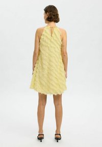 Yellow halter dress with layered fringe texture, open back, and a keyhole detail, above knee length, paired with black heeled sandals.