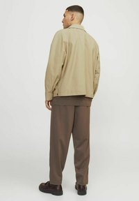 Beige bomuldsjakke med en afslappet pasform, sidelommer og rygventilation, parret med brune vidde bukser og mørke sko.