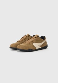 Braune Wildleder-Sneaker mit einer strukturierten Oberseite, kontrastierenden weißen Swoosh-Details, schwarzen Akzenten und einer Gummisohle mit einem gemusterten Profil.