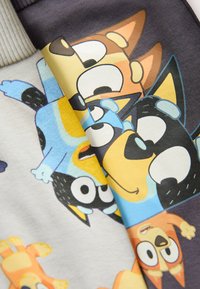 Visages de dessins animés de plusieurs chiens souriants en bleu, noir, jaune, marron et orange sur un tissu plié ou des vêtements.