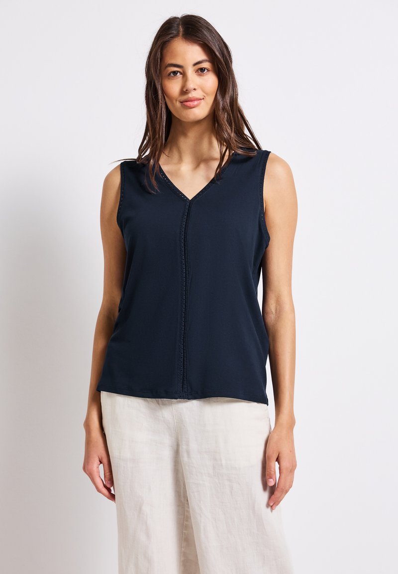 Top senza maniche blu navy in morbido tessuto, con scollo a V, dettagli con cuciture centrali e vestibilità rilassata. Abbinato a pantaloni di lino chiari.