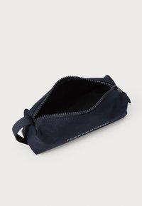 Marinblå dragkedjepåse i slitstarkt material, med en logo och en tygslits för enkel bärning. Interiören är svart.