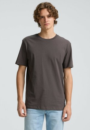 Gray cotton crew-neck t-shirt with short sleeves, featuring a relaxed fit and a small logo tag at the bottom side, paired with light blue jeans.