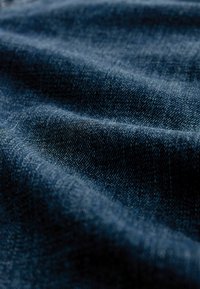 Dunkelblaues Denimgewebe mit einer strukturierten Oberfläche, die sichtbare Webmuster und einen subtilen Glanz durch Falten und Knicke aufweist.