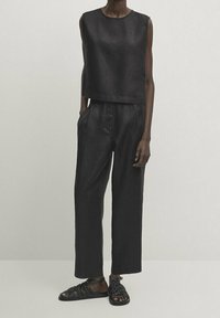 Musta hihaton crop-top ja leveälahkeiset housut, jotka on valmistettu teksturoidusta kankaasta, yhdistettynä mustiin remmisandaaleihin. Yksinkertainen muotoilu, ei näkyviä kuvioita.