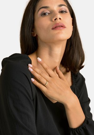 Gold ring with a small stone, worn on a hand with light pink nails. Black top with a soft texture and gathered sleeve detail.