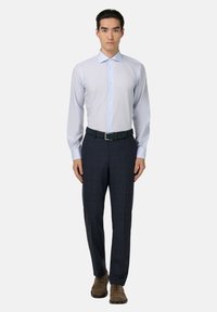 Lichtblauw overhemd met lange mouwen en een kraag, gecombineerd met donker geruite broeken en bruine veterlaarzen. De opvallende riem is donkergroen met een rechthoekige gesp.