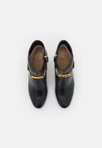 Svarta läderankelskor med spetsig tå och detaljer i gyllene kedja runt vristen. Slät textur med sidodragkedja.