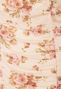 Tissu crème avec un motif floral rose et beige, présentant une texture froncée et plissée le long des coutures verticales.