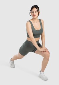 Conjunto atlético verde que incluye una camiseta sin mangas ajustada y pantalones cortos de tela suave. Zapatillas deportivas blancas con una suela texturizada. Diseño simple y funcional.