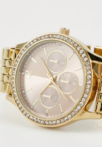 Gold-tone watch with a round case, pink metallic dial, three subdials, and a crystal-accented bezel. Metal link bracelet.