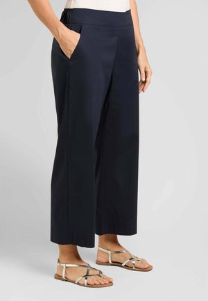 Persona che indossa pantaloni larghi corti blu navy con vita elasticizzata, top bianco e sandali bassi marrone chiaro con cinturini.