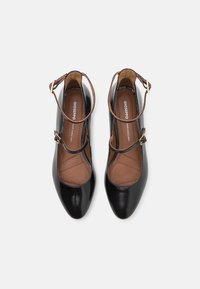 Scarpe Mary Jane in vernice nera con punta arrotondata, cinturino alla caviglia e soletta imbottita beige con dettagli trapuntati.