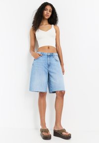 Világoskék farmer rövidnadrág, laza fit, rojtos szegéllyel és öt zsebbel. Fehér bordázott crop top-pal és barna platform szandállal párosítva.