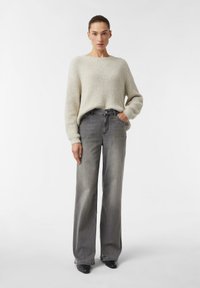Jasnoszary dziergany sweter o prążkowanej fakturze, zestawiony z szarymi, wyblakłymi dżinsami z wysokim stanem i szerokimi nogawkami oraz czarnymi butami na obcasie.