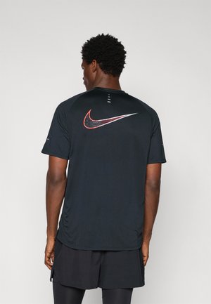 T-shirt de sport noir à manches courtes avec logo Nike rouge et blanc au dos. Tissu léger, texture lisse et ourlet arrière légèrement allongé.