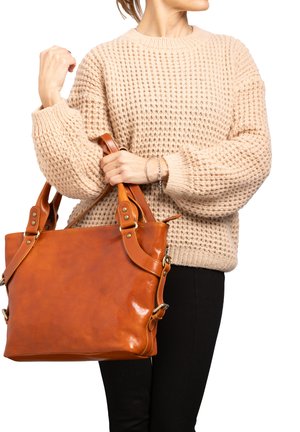 Borsa tote in pelle marrone con tracolle regolabili, finitura lucida e hardware in metallo, abbinata a un maglione lavorato a maglia beige e pantaloni neri.