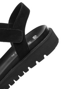 Sort sandal med en tyk ribbede sål, justerbar velcrolukning og polstret indersål designet til komfort og afslappet brug.